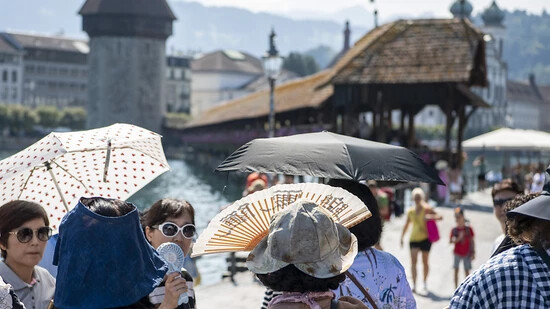 Touristen aus Asien trotzen der Hitze vor der Kapellbruecke in der Stadt Luzern am Dienstag, 22. August 2023. (KEYSTONE/Urs Flueeler).