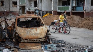 Zwei Jungen schieben ihre Fahrräder an zerstörten Autos und Wohngebäuden in Tschernihiw vorbei. Foto: Michal Burza/ZUMA Press Wire/dpa