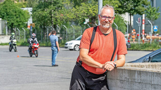 Volle Unterstützung: Motorradfahrlehrer Bruno Schlegel posiert kurz für die Fotografin, während sein Fahrschüler (in grüner Montur im Hintergrund) auf dem Areal des Strassenverkehrsamts in Chur die Führerscheinprüfung ablegt.